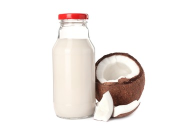 Glass bottle of delicious vegan milk and coconut pieces on white background