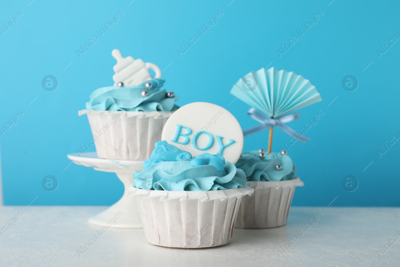 Photo of Baby shower cupcakes with toppers on white table against light blue background