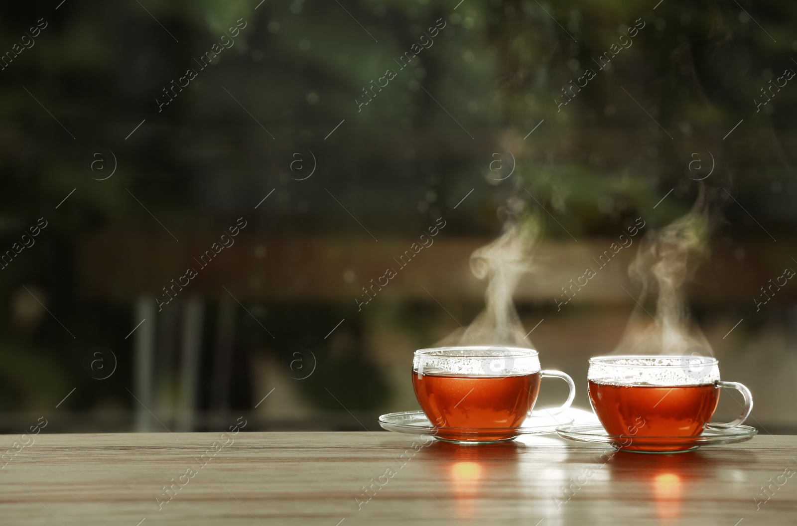 Photo of Cups of hot tea on wooden table against blurred background, space for text