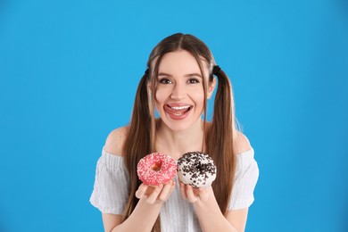 Beautiful young woman with donuts on light blue background