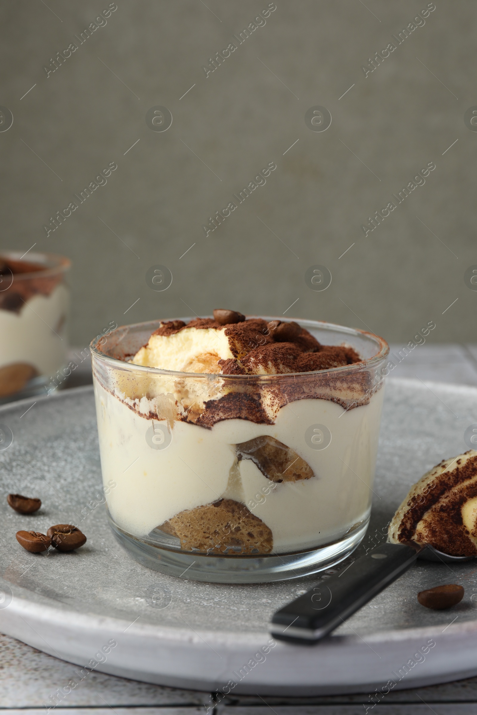 Photo of Delicious tiramisu in glass, coffee beans and spoon on table