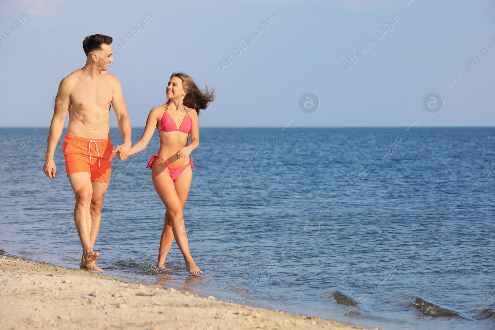 Photo of Young woman in bikini spending time with her boyfriend on beach. Lovely couple