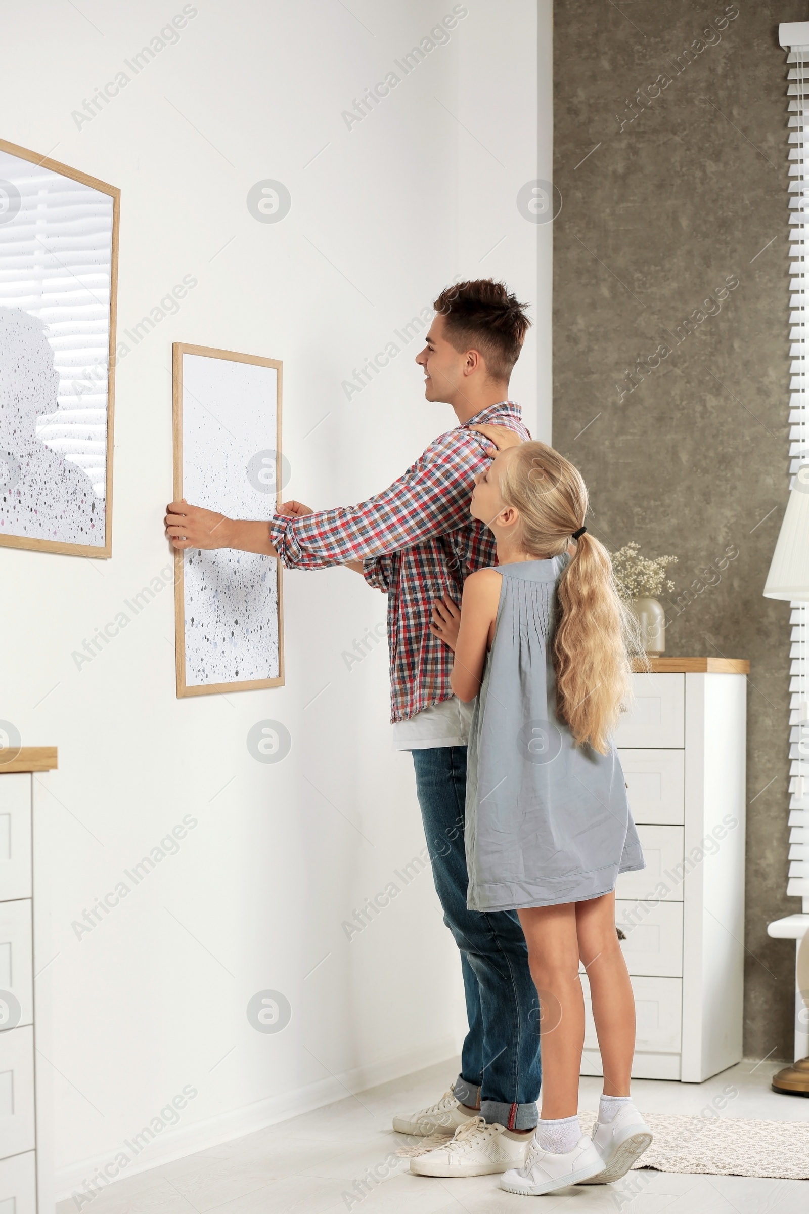 Photo of Father and daughter hanging picture on wall at home