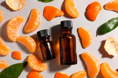 Photo of Aromatic tangerine essential oil in bottles, leaves and citrus fruit on grey table, flat lay
