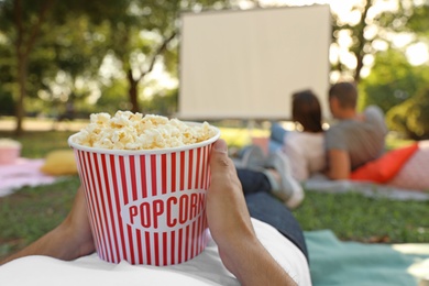 Young man with popcorn watching movie in open air cinema, closeup. Space for text