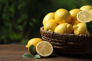 Photo of Fresh lemons in wicker basket on wooden table. Space for text