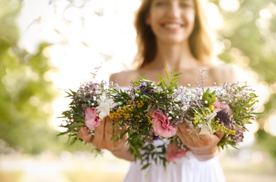 Photo of Young woman holding wreath made of beautiful flowers outdoors, focus on hands
