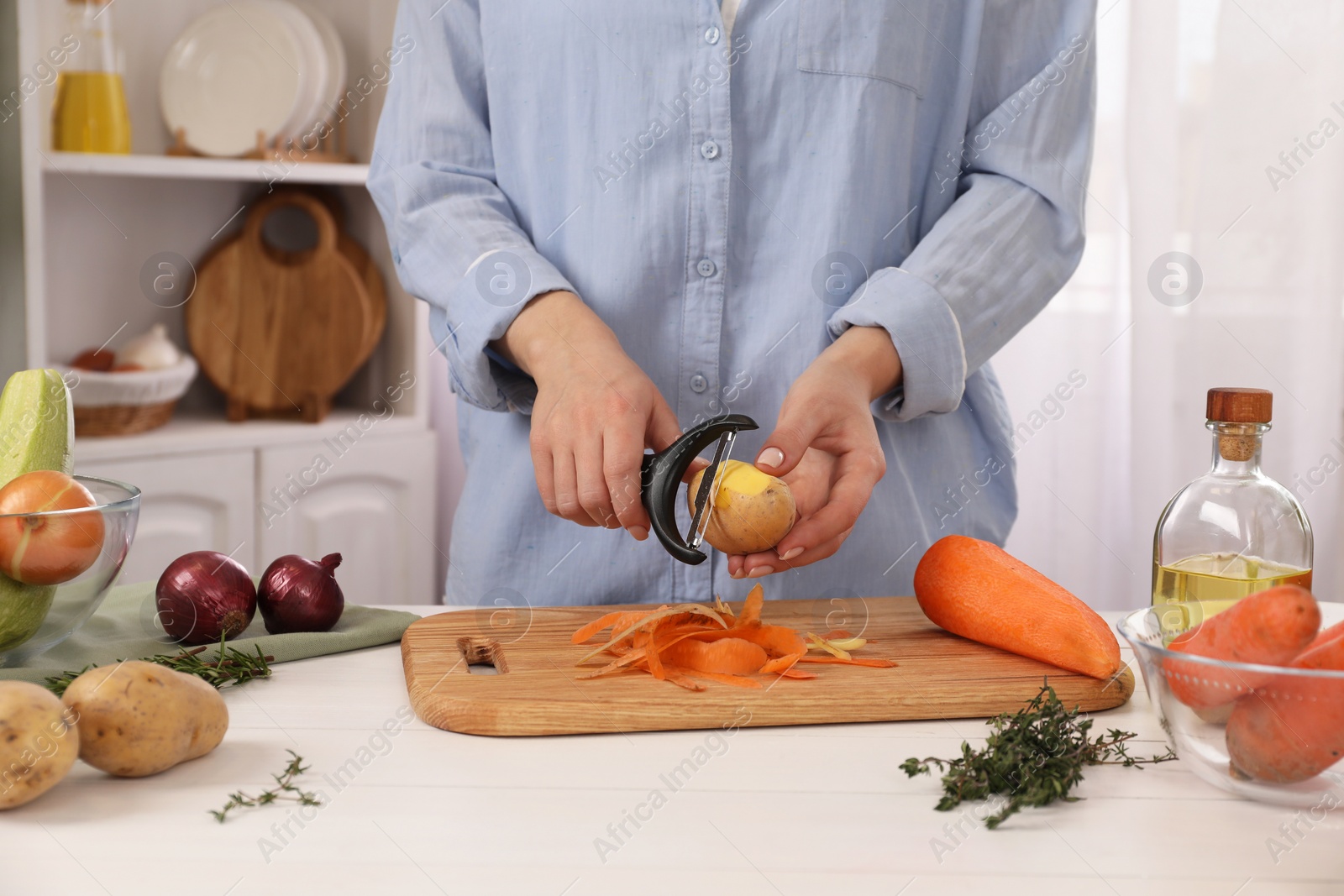 Photo of Woman peeling fresh potato at white wooden table indoors, closeup