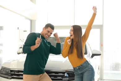 Happy couple with car key in modern auto dealership