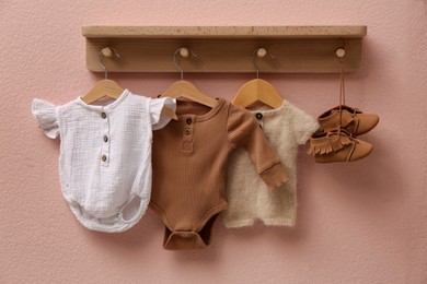 Photo of Wooden rack with cute baby clothes and shoes on pink wall indoors
