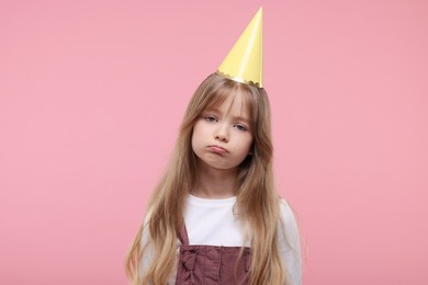 Photo of Bored little girl in party hat on pink background