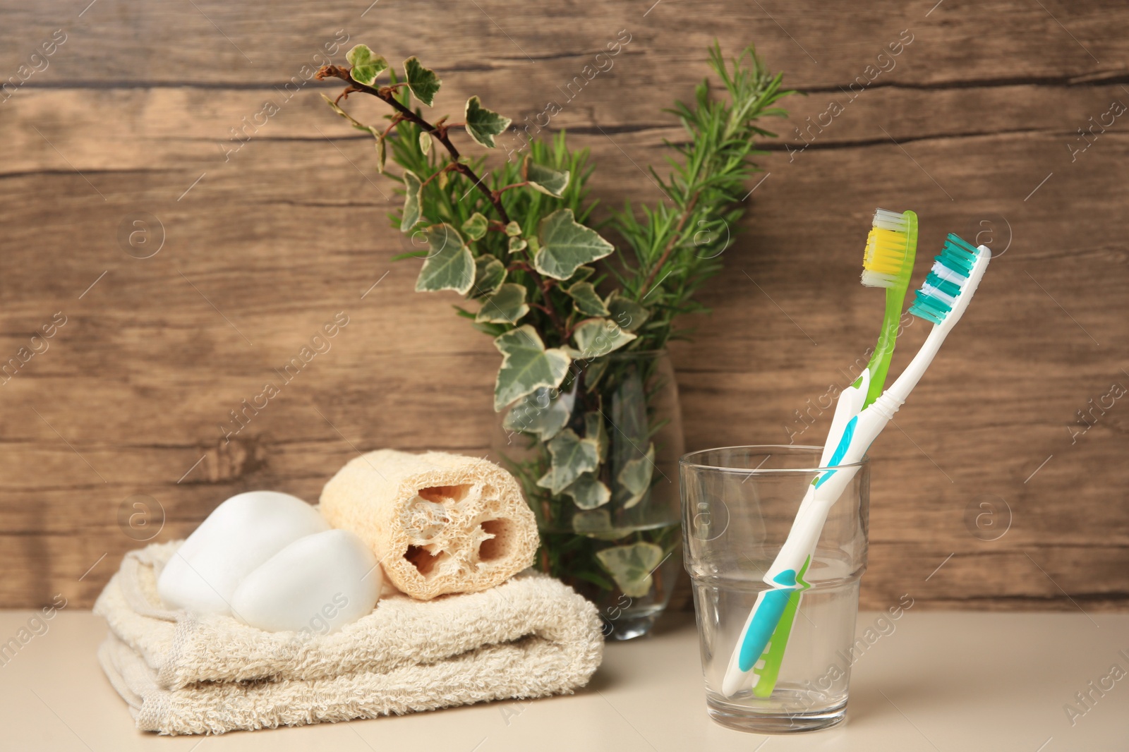 Photo of Toothbrushes in glass, towel, loofah and stones on beige table