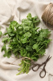 Photo of Fresh green cilantro, twine and scissors on white fabric, flat lay