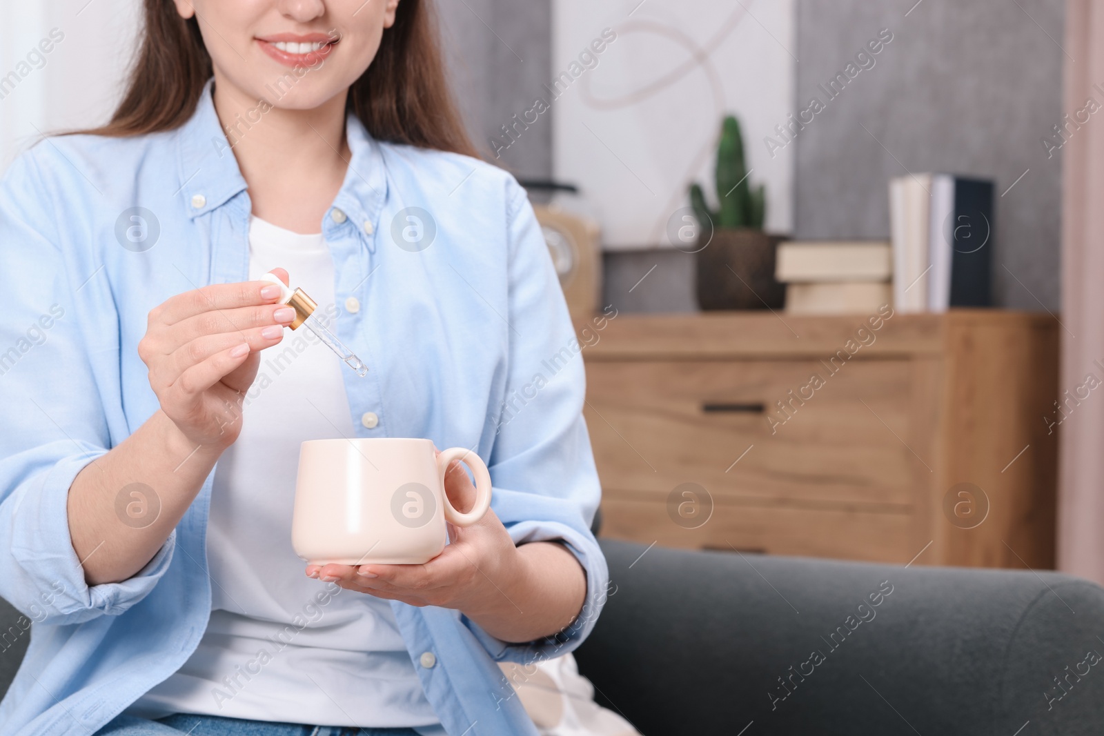 Photo of Woman dripping food supplement into cup indoors, closeup. Space for text