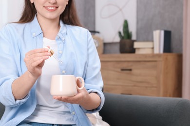 Photo of Woman dripping food supplement into cup indoors, closeup. Space for text