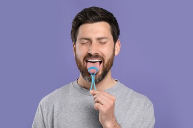 Photo of Handsome man brushing his tongue with cleaner on violet background