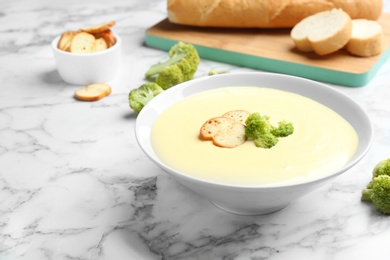 Photo of Bowl of cheese cream soup with broccoli and croutons served on white marble table