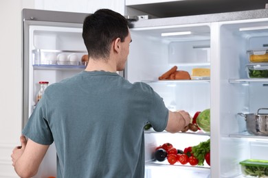 Man near refrigerator in kitchen at home, back view