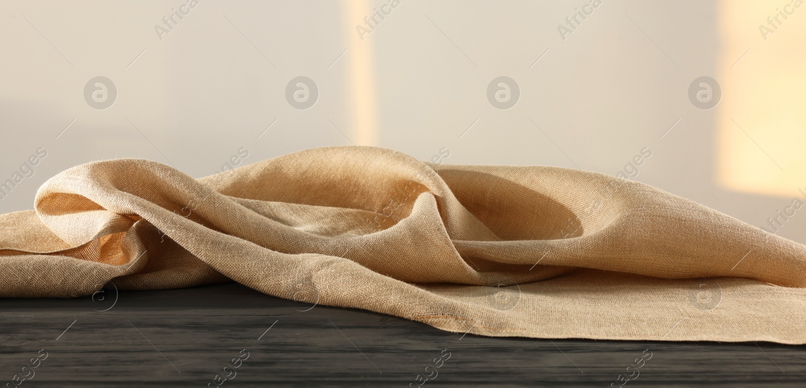 Photo of Natural burlap fabric on wooden table against light background. Space for text