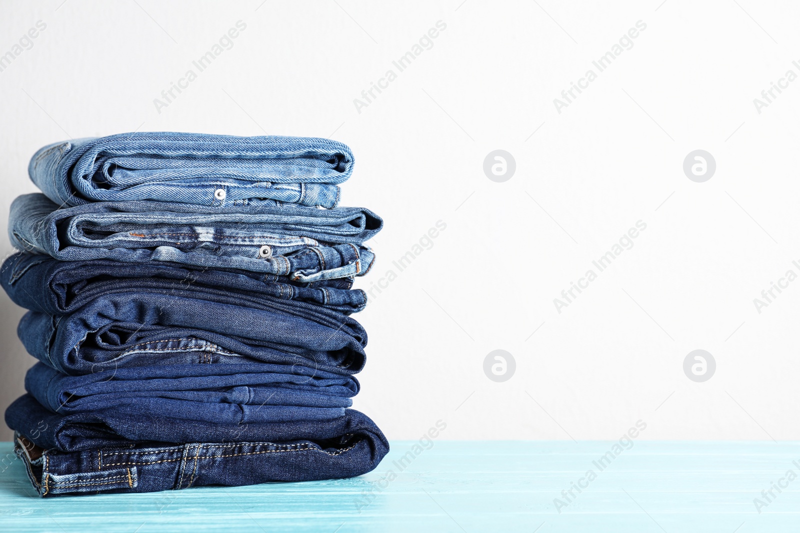 Photo of Stack of different jeans on blue wooden table. Space for text