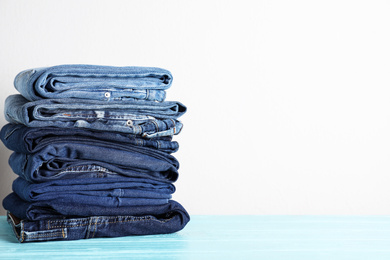 Stack of different jeans on blue wooden table. Space for text