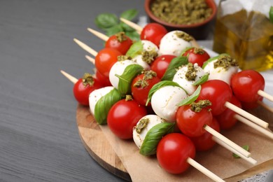 Caprese skewers with tomatoes, mozzarella balls, basil and pesto sauce on grey wooden table, closeup. Space for text