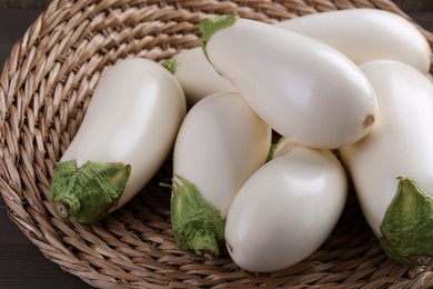 Photo of Fresh white eggplants in wicker basket on wooden table, closeup