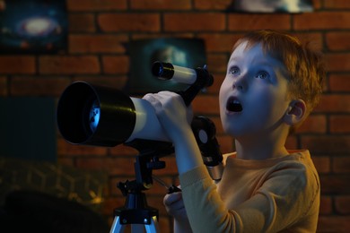 Photo of Emotional little boy using telescope to look at stars in room