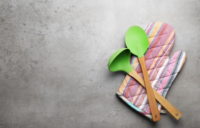 Photo of Different kitchen utensils and oven mitten on grey background, top view with space for text