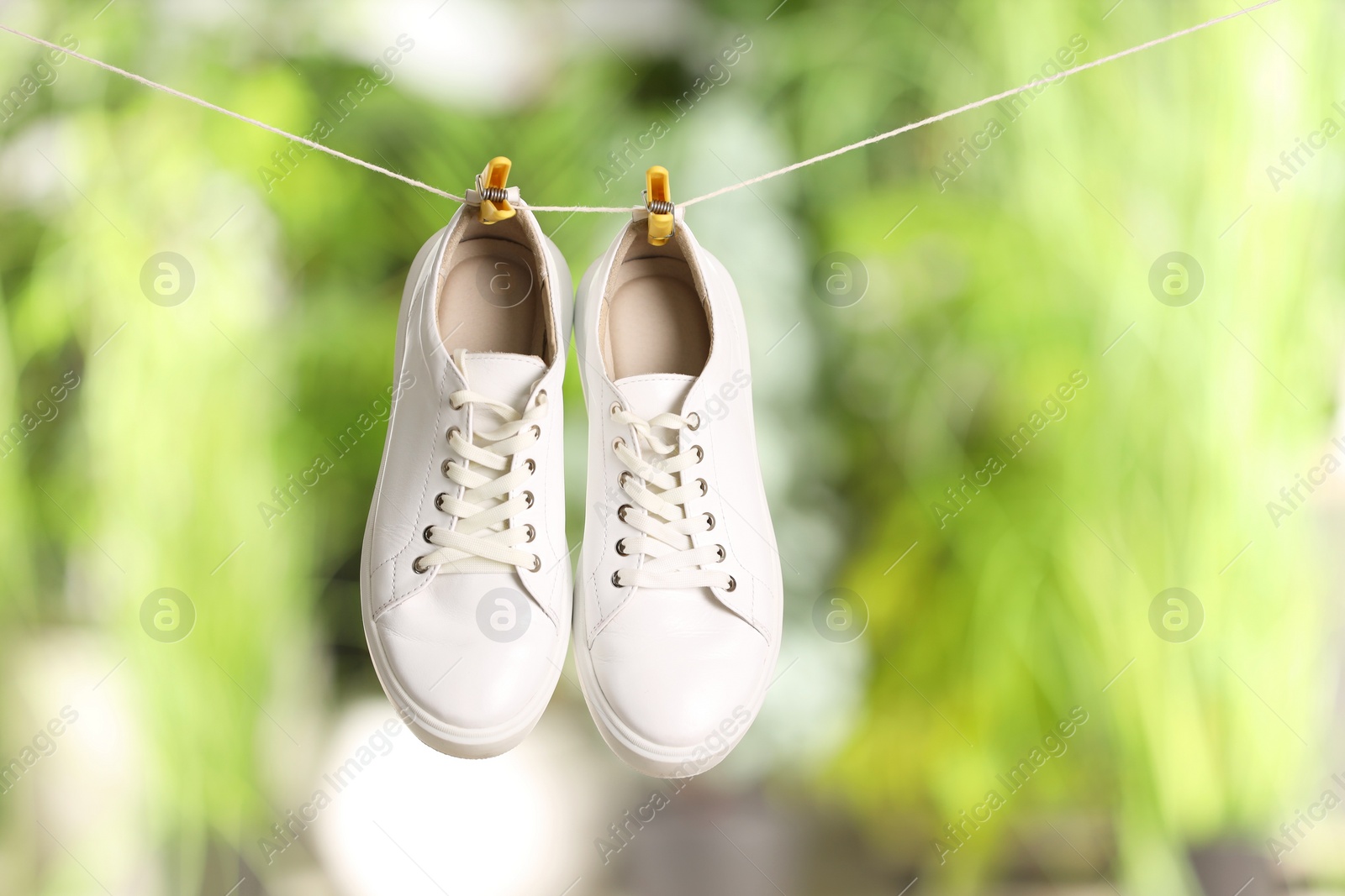 Photo of Stylish sneakers drying on washing line against blurred background