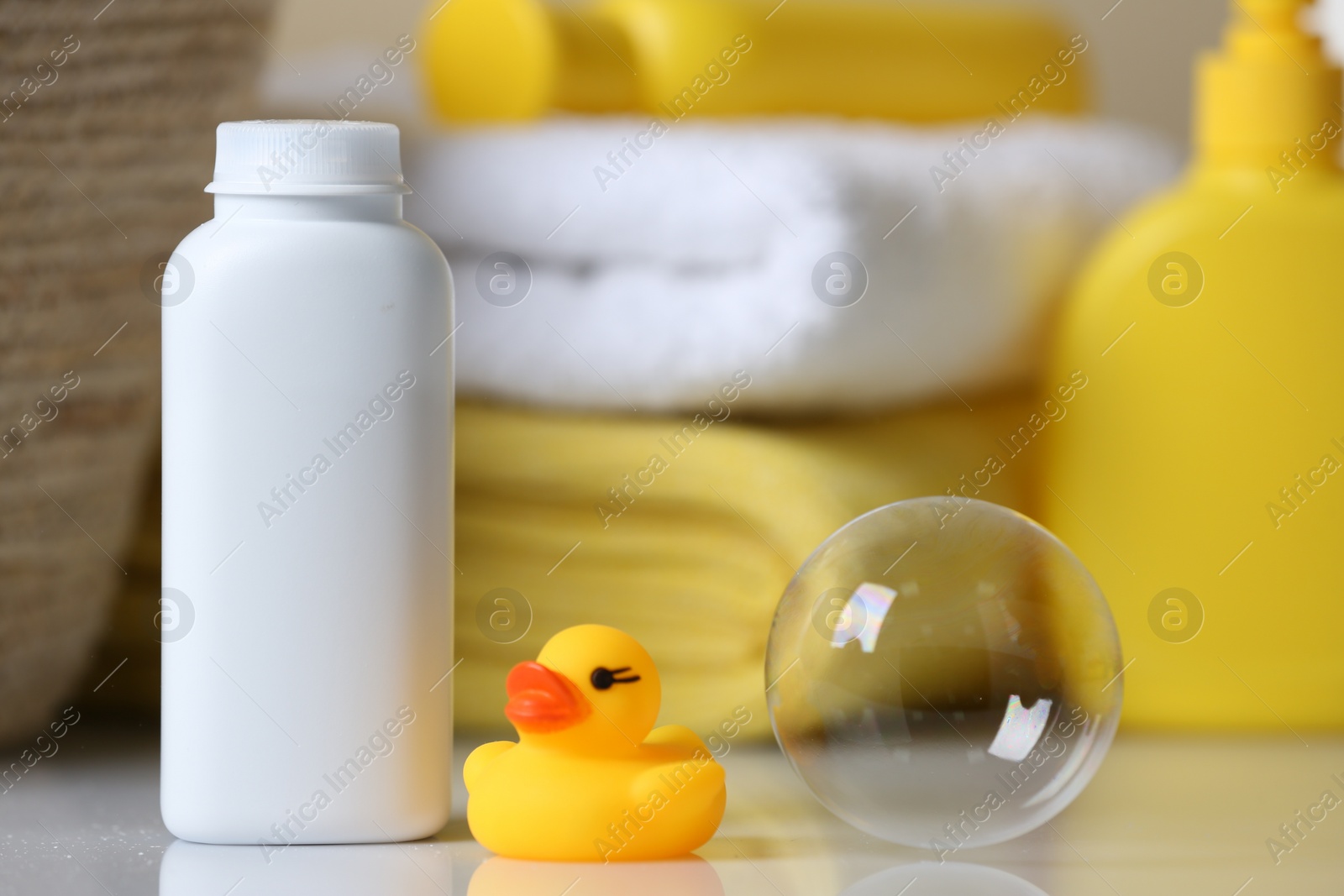 Photo of Bottle of dusting powder and rubber duck on white table, space for text. Baby cosmetic product