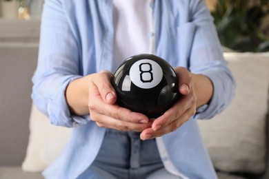 Photo of Woman holding magic eight ball indoors, closeup