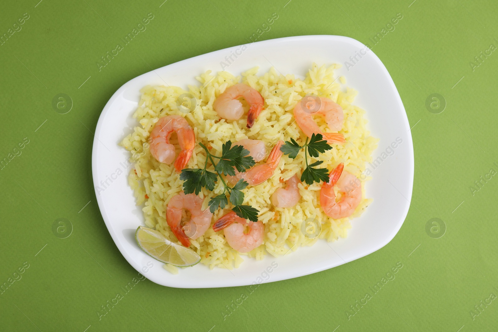 Photo of Delicious risotto with shrimps, lime and parsley on light green background, top view