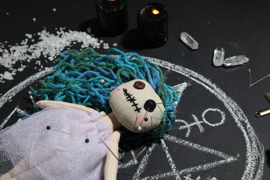 Female voodoo doll with pins surrounded by ceremonial items on black background