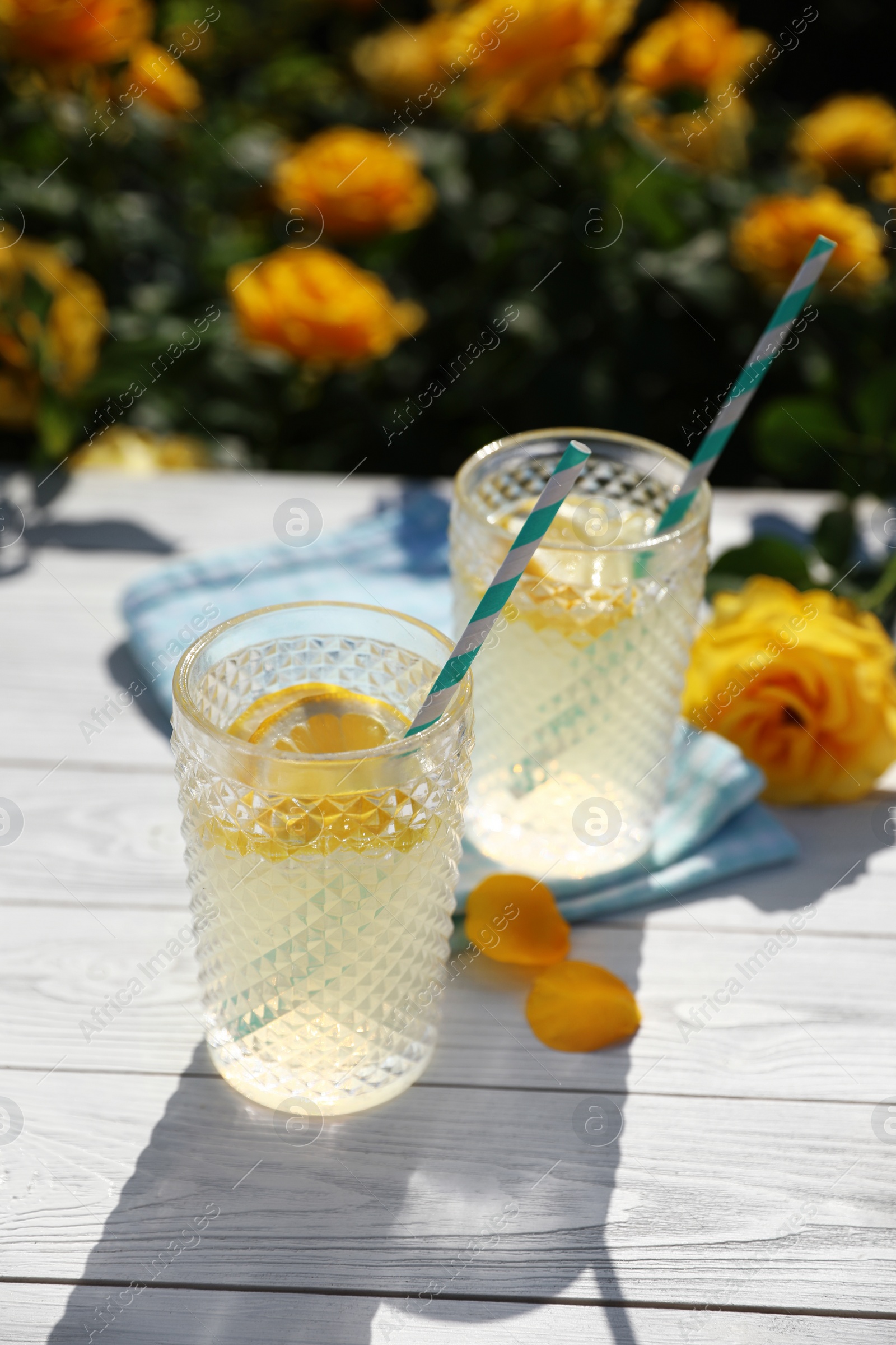 Photo of Glasses of refreshing lemonade on white wooden table in rose garden