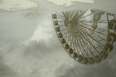 Reflection of Ferris wheel in puddle on asphalt outdoors