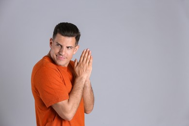 Photo of Greedy man rubbing hands on grey background, space for text