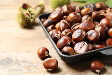 Photo of Delicious roasted edible chestnuts in baking dish on wooden table, closeup