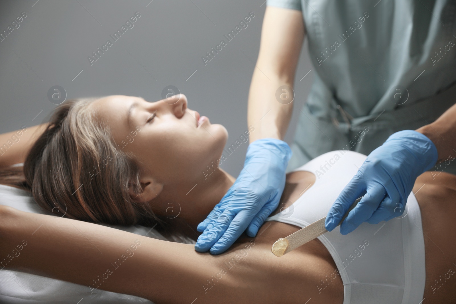 Photo of Young woman undergoing hair removal procedure of armpits with sugaring paste in salon