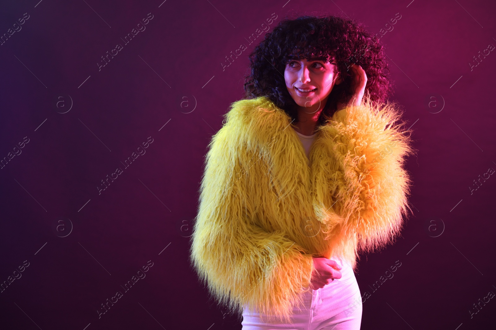 Photo of Beautiful young woman in yellow fur coat and sunglasses on color background in neon lights