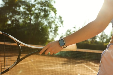 Photo of Woman wearing modern smart watch during training on tennis court, closeup