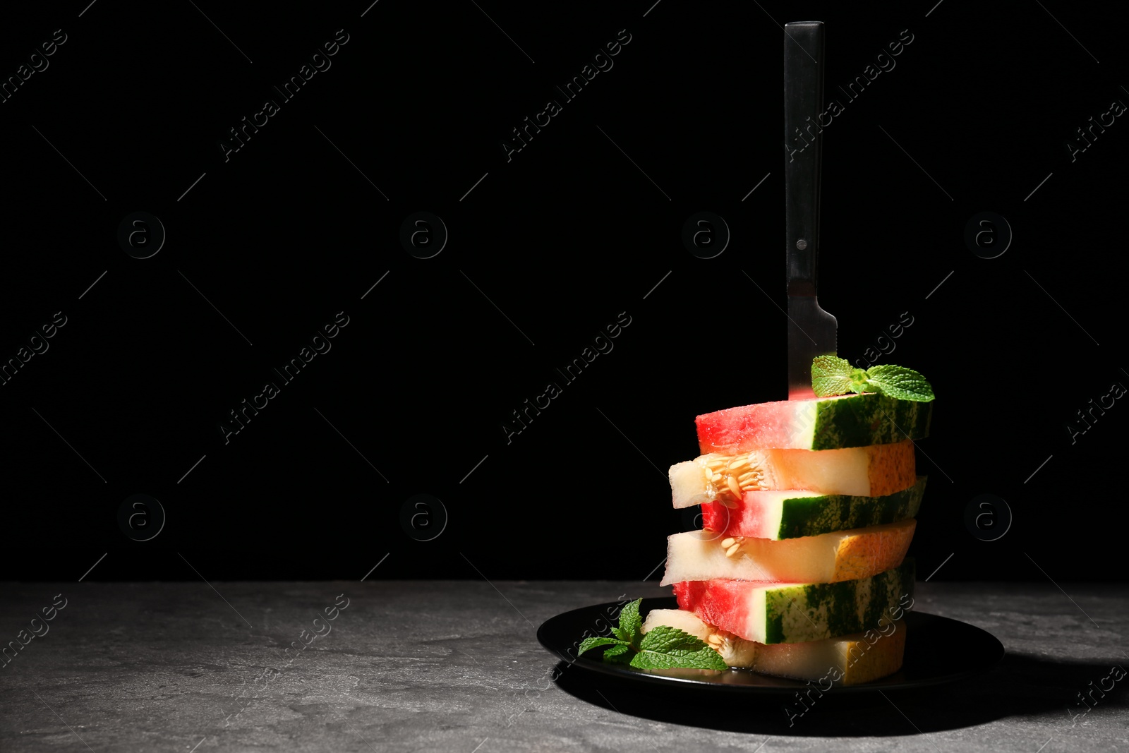 Photo of Stacked watermelon and melon slices on plate against black background. Space for text
