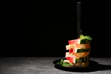 Stacked watermelon and melon slices on plate against black background. Space for text