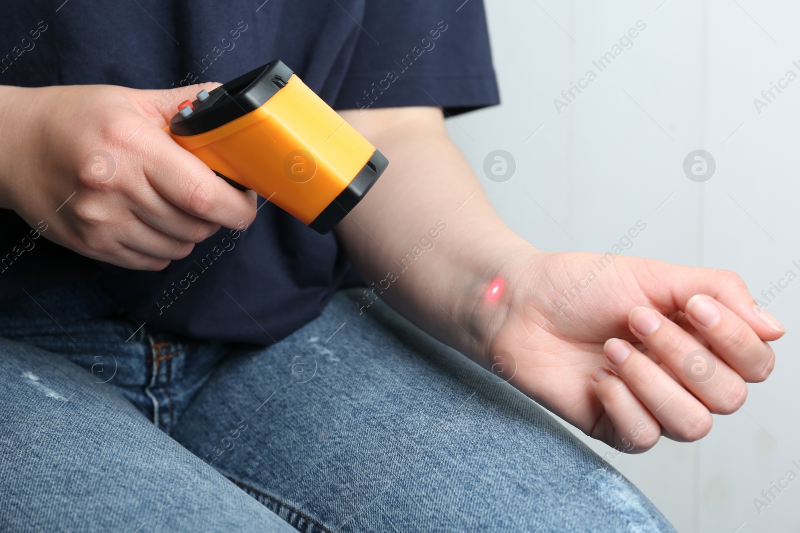 Photo of Woman measuring temperature with non contact infrared thermometer on light background, closeup