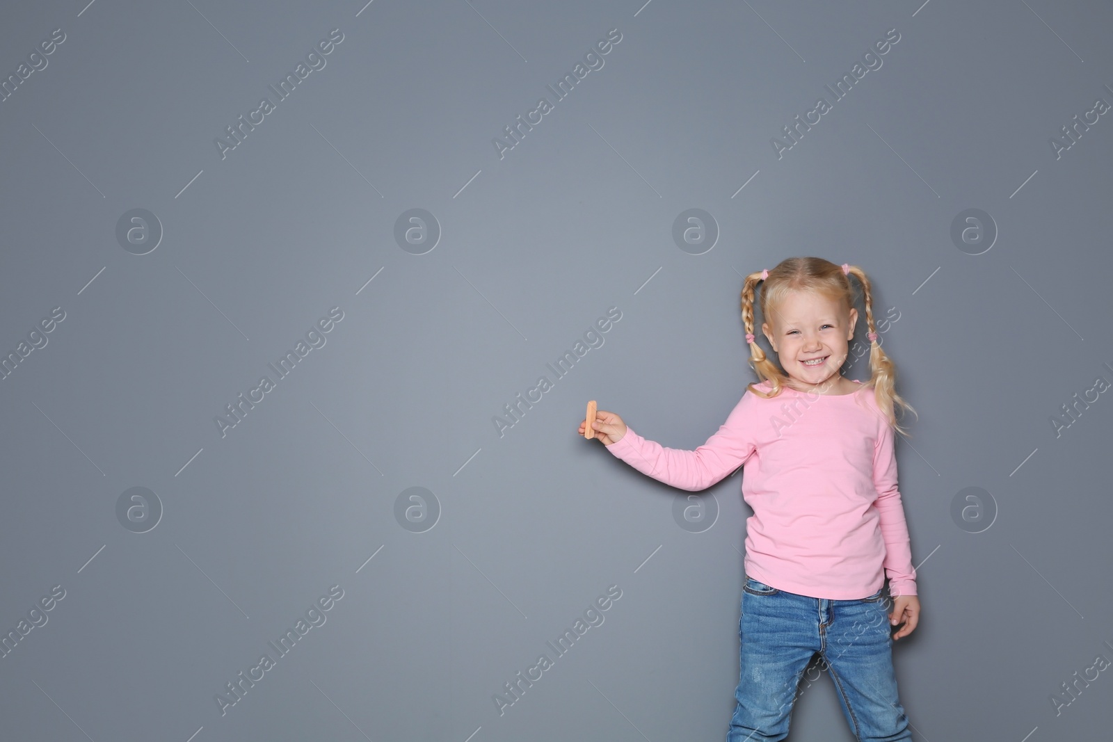 Photo of Little girl with colorful chalk standing against gray background. Space for design