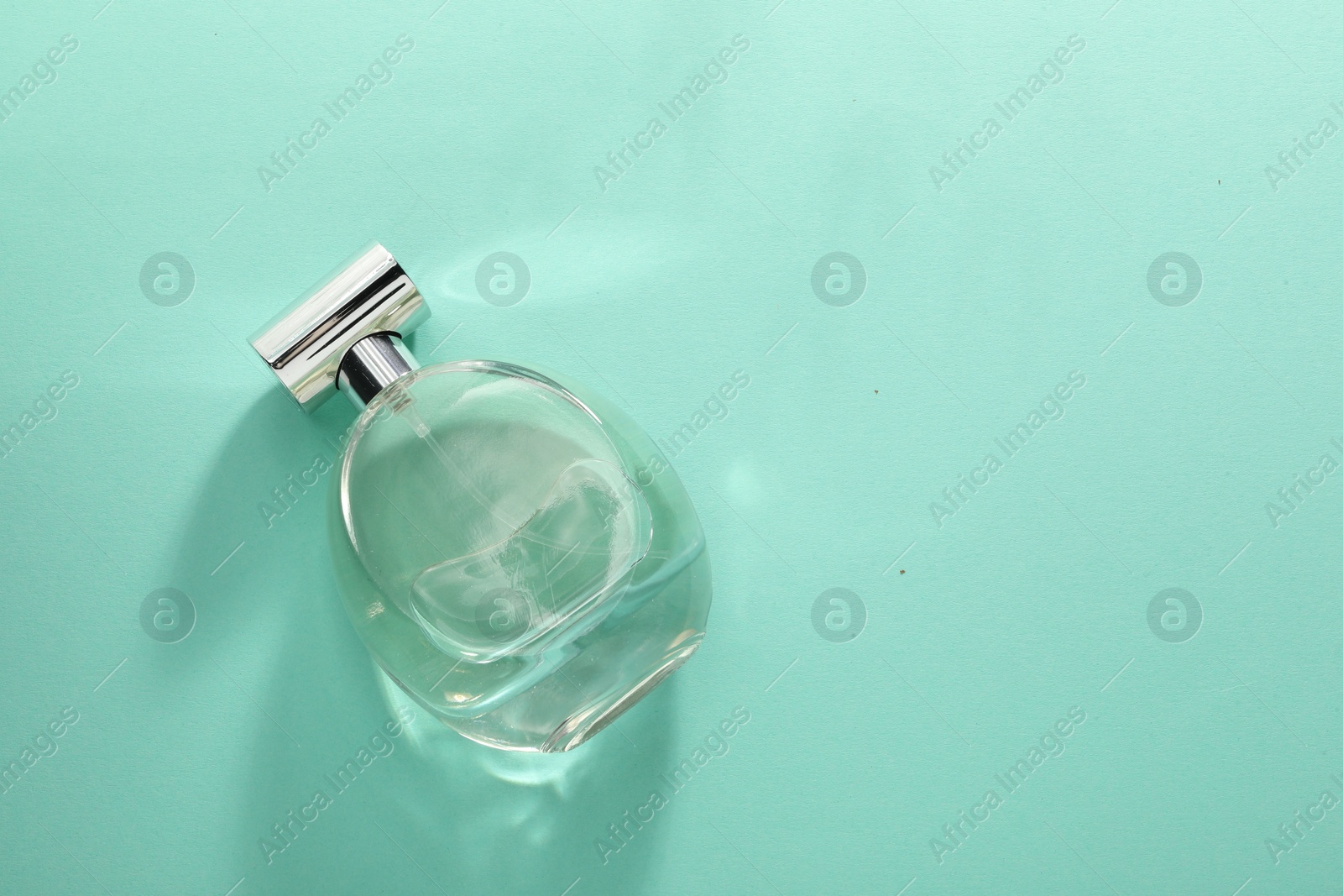 Photo of Luxury perfume in bottle on turquoise background, top view. Space for text