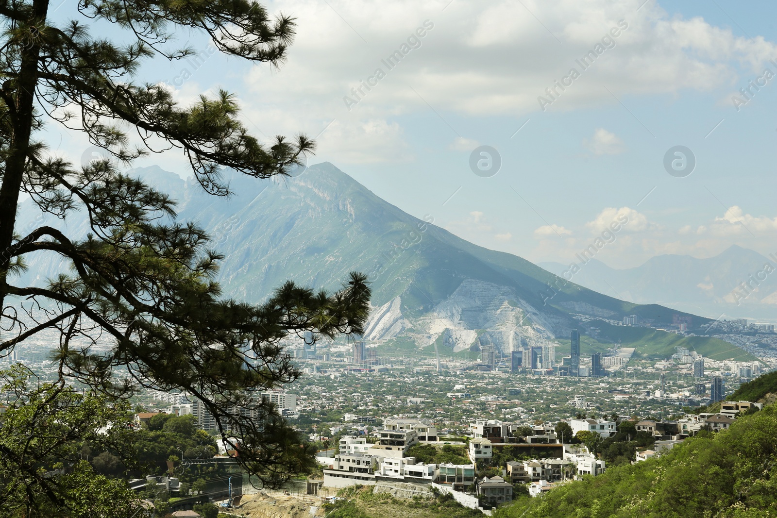 Photo of Picturesque view of trees, buildings and mountains under beautiful sky in city