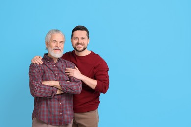 Happy son and his dad on light blue background, space for text