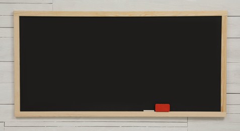 Photo of Clean black chalkboard hanging on white wooden wall