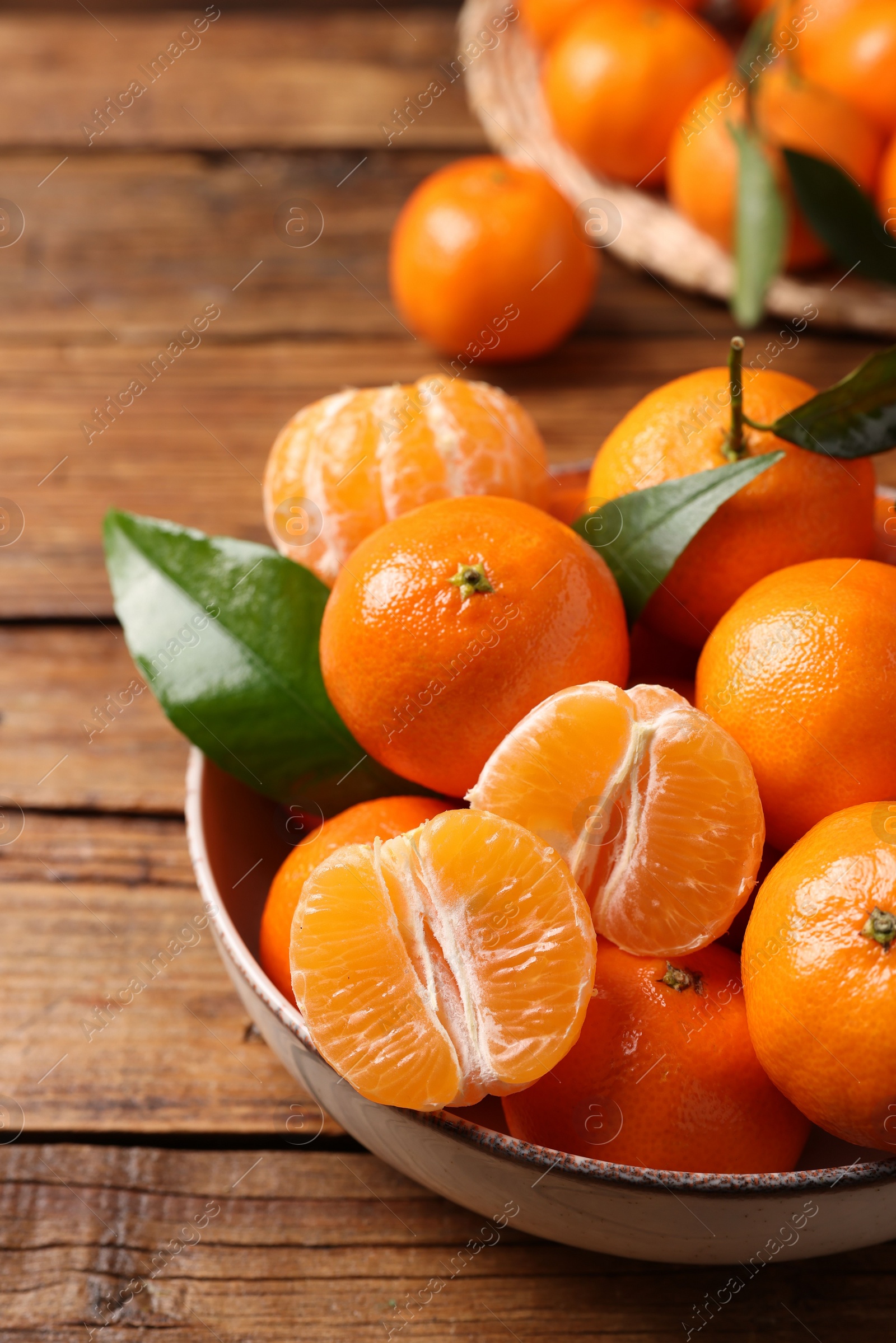 Photo of Fresh tangerines with green leaves in bowl on wooden table, closeup